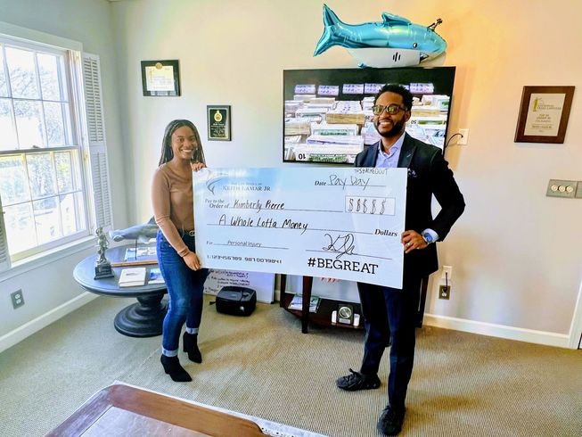 Two people holding a large check. Indoor setting with shark balloon and decor.