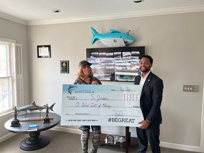 Woman and man holding a large check, smiling, indoors with shark decor.