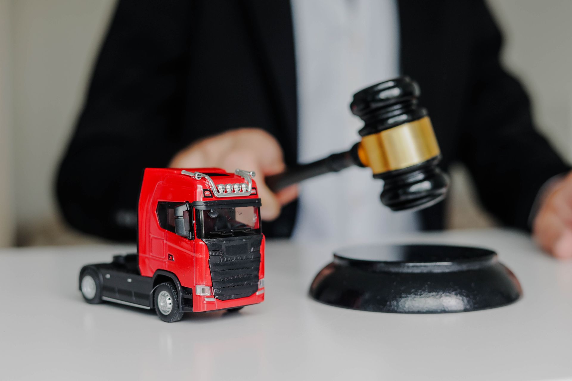A truck accident lawyer in a suit, hitting a gavel with a toy cargo truck on the table.