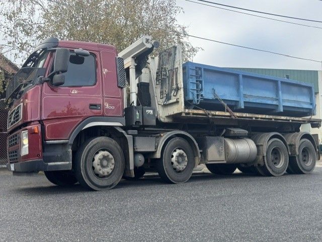 Maroon dump truck with blue bed parked on a roadside under overcast sky