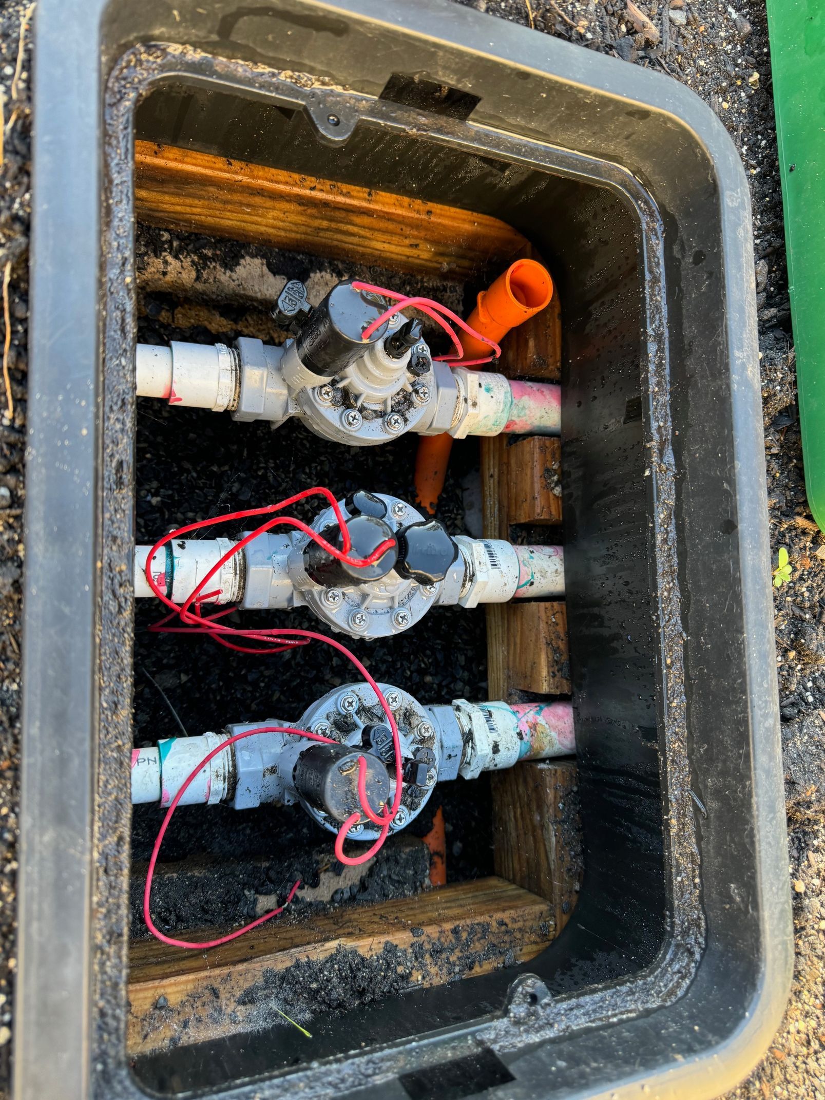 Three sprinkler valves inside a black plastic box, with red wires connected to the top.