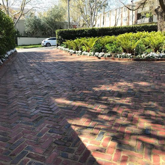 Brick driveway with herringbone pattern, flanked by hedges and greenery.