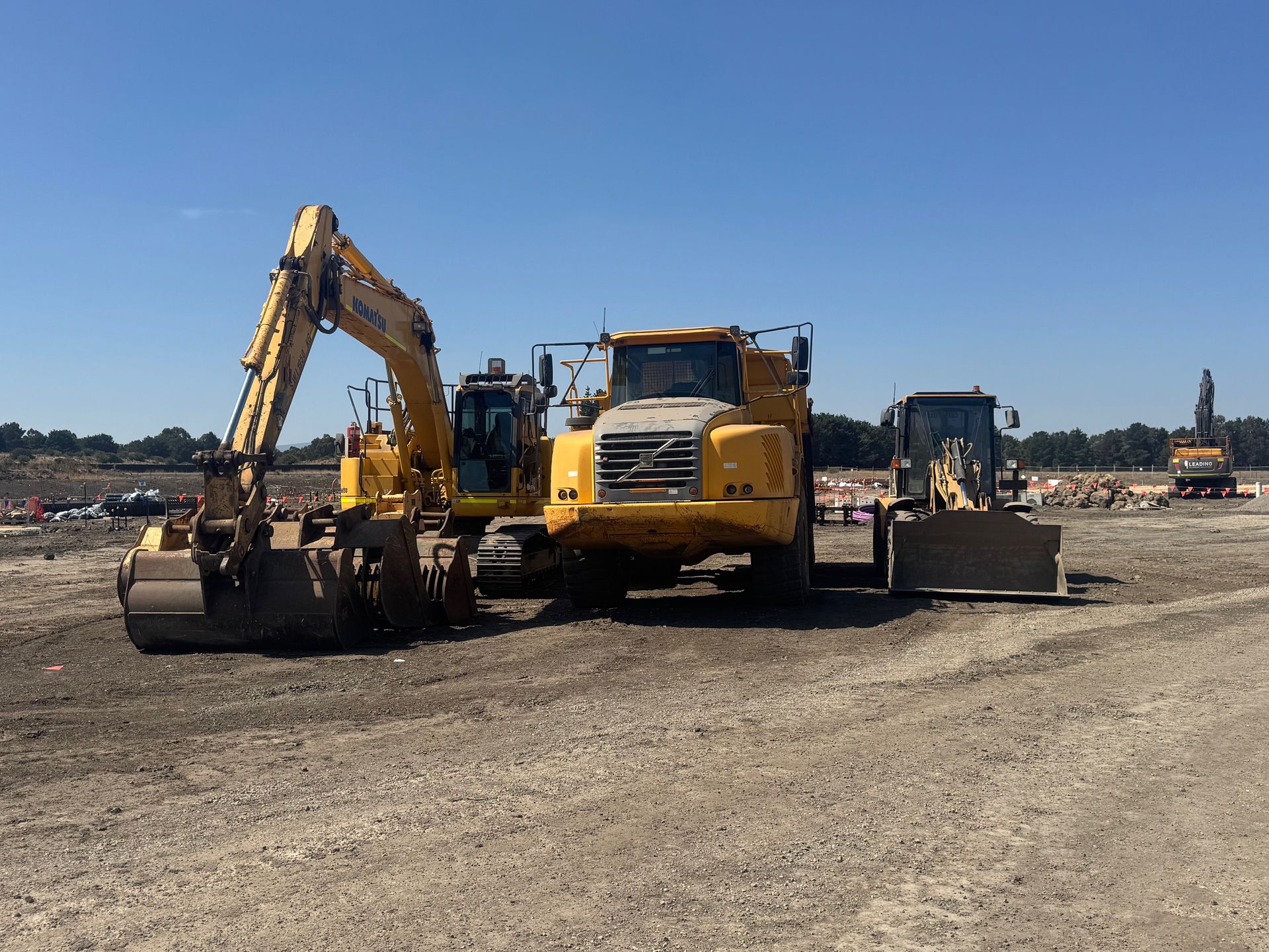 Yellow construction equipment on a dirt lot under a clear blue sky.