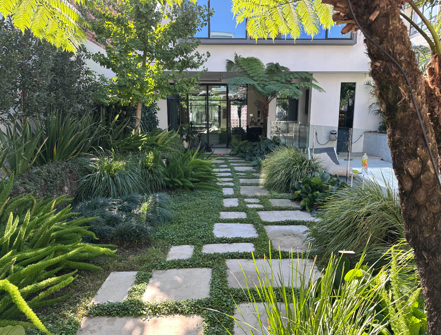 Stone path through a lush garden leading to a white house with trees and greenery