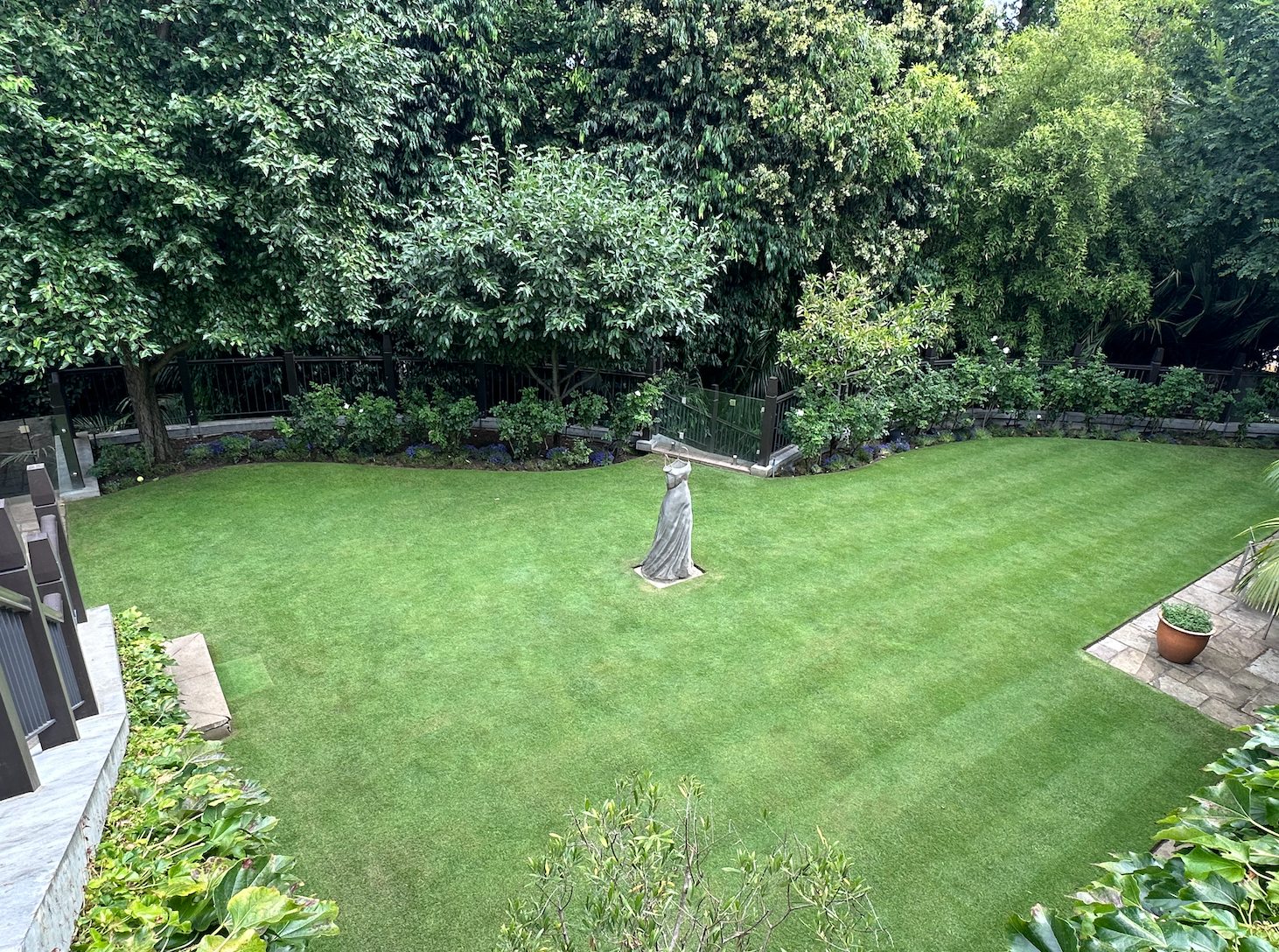 Lush green backyard lawn bordered by dense trees and shrubs, with a small stone feature in the center.