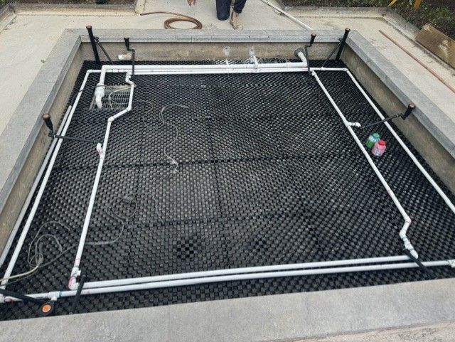 Rectangular black pool cover in a concrete patio area, with white pipes and a small pink object at right