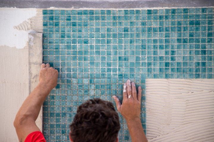 Worker installing blue mosaic tiles on a wall