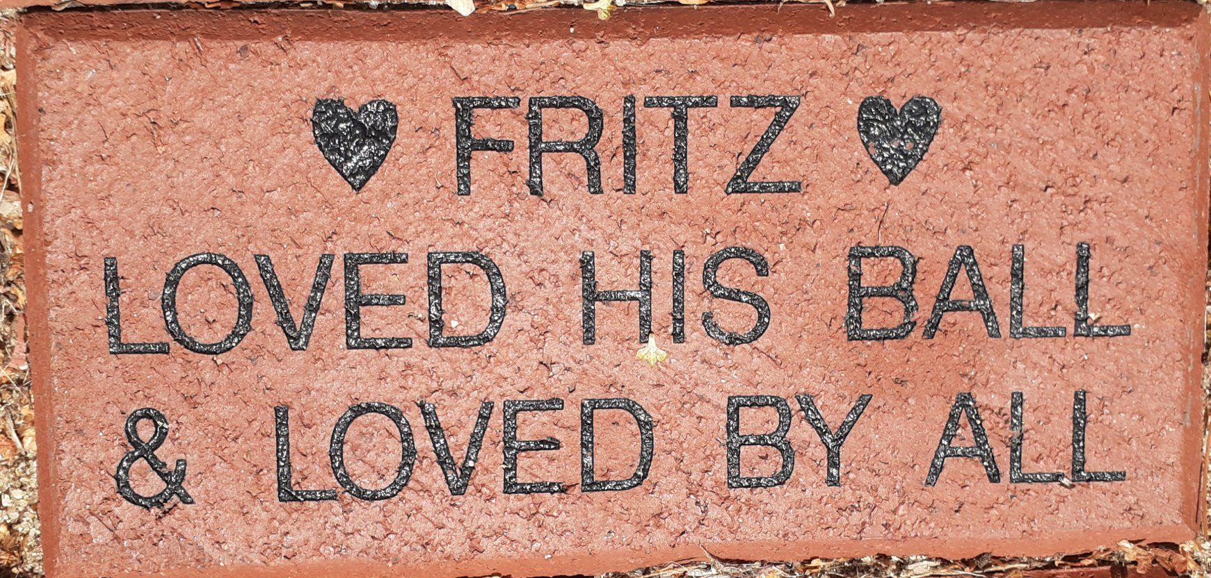 A reddish-brown memorial brick inscribed with 