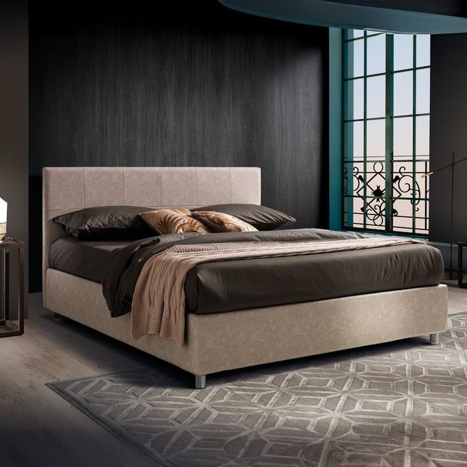 Un letto imbottito beige con lenzuola scure e un plaid color cuoio, posizionato in una stanza moderna con una parete nera e una finestra.