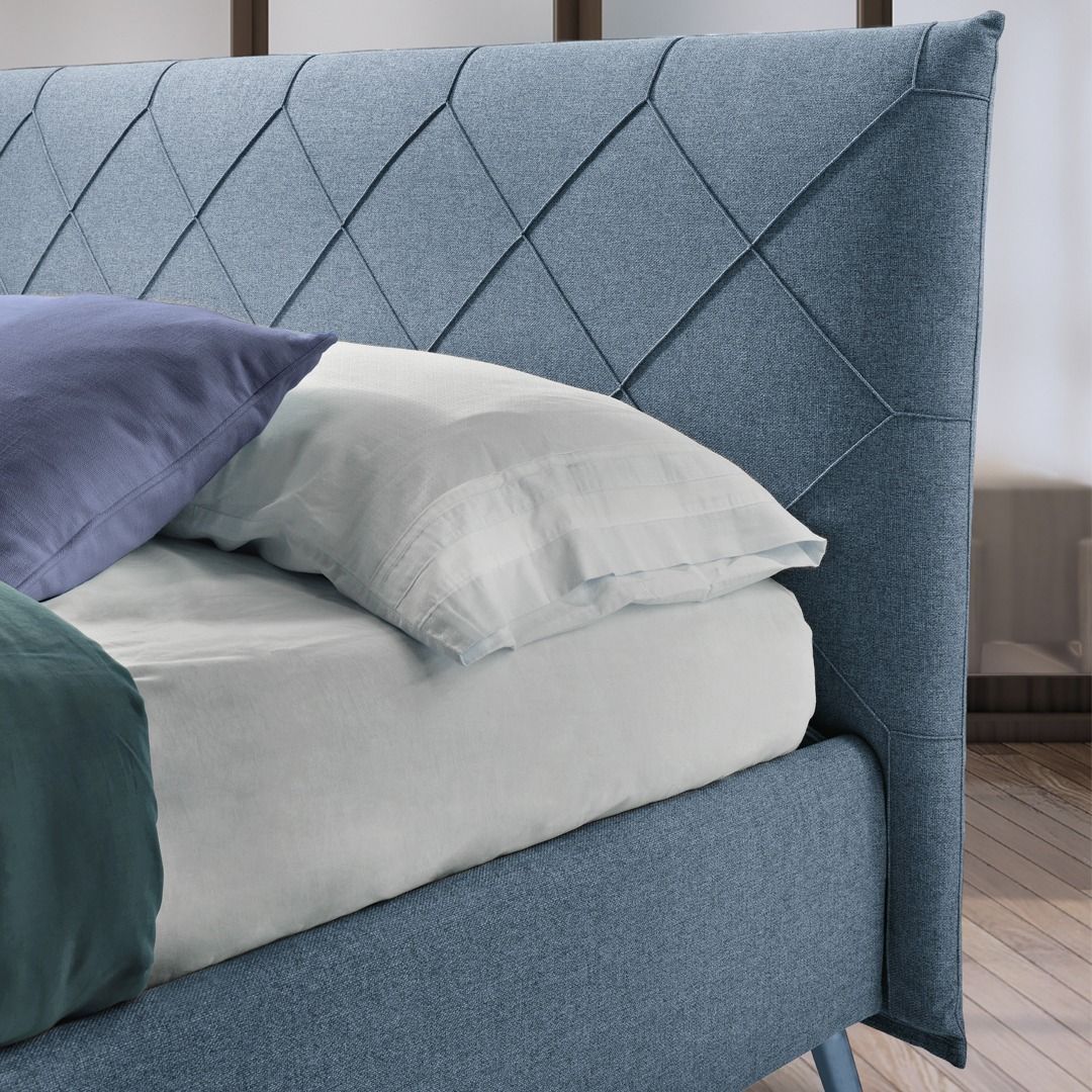 Una struttura letto imbottita blu con testiera trapuntata a rombi, lenzuola bianche e due cuscini.