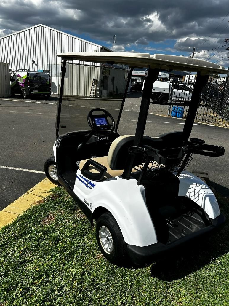 A White Golf Cart Is Parked on The Grass in A Parking Lot — DTM Tamworth in Tamworth, NSW