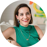Woman smiles at the camera; wearing white shirt and drop earrings. Bright background with artwork.