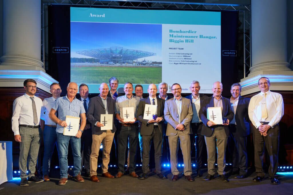 A group of men are standing in front of a large screen holding awards.