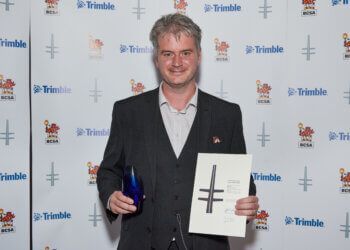 A man in a suit is holding an award and a piece of paper with a cross on it.