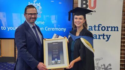 A man in a suit is holding a framed picture of a woman in a graduation cap and gown.