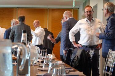 A group of men are standing around a table at a conference.