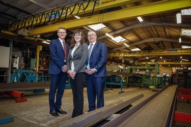 Three people are standing next to each other in a factory.