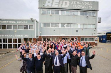 A large group of people are standing in front of a building that says reid structural engineers.