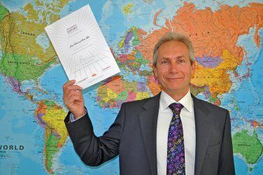 A man in a suit and tie is holding a piece of paper in front of a map of the world.