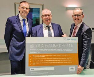 Three men in suits and ties are holding a sign that says the uk steel charter.