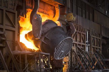 A person is pouring molten metal into a ladle in a factory.