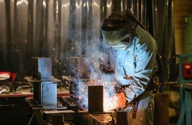 A man is welding a piece of metal in a factory.