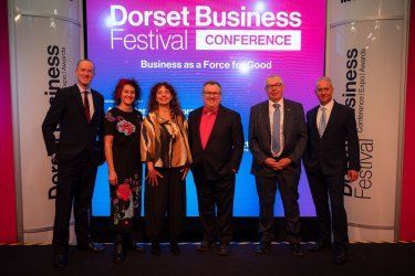 A group of people standing in front of a screen that says dorset business festival conference.