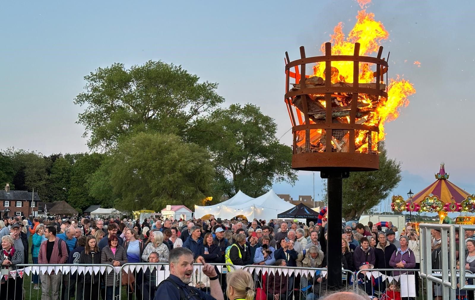 A crowd of people are gathered around a torch with flames coming out of it.