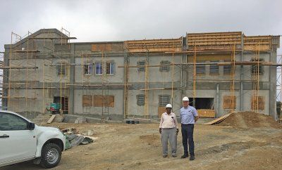 Two men are standing in front of a  Reidsteel  school building under construction.