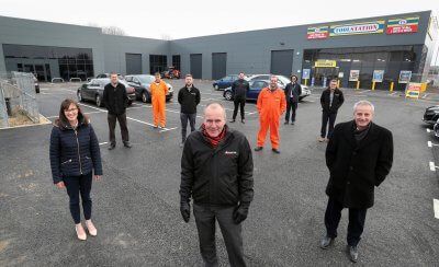 A group of people are standing in a parking lot in front of a building.