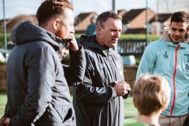 A group of men are standing on top of a soccer field talking to each other.