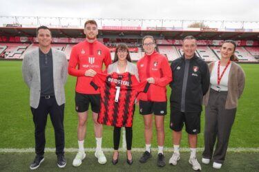 A group of people are standing on a soccer field holding a jersey.