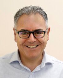 A man wearing glasses and a blue shirt is smiling for the camera.