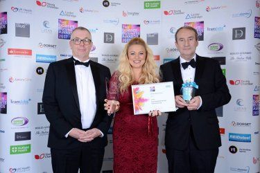 A woman in a red dress is standing between two men in tuxedos holding a certificate.