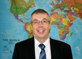 A man in a suit and tie is standing in front of a map of the world.