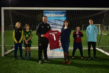 A group of people are standing in front of a soccer goal holding a jersey.