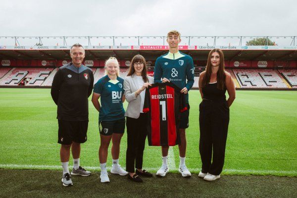 A group of people standing on a soccer field holding a jersey with the number 1 on it.