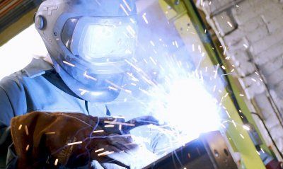 A man wearing a welding helmet is welding a piece of metal.