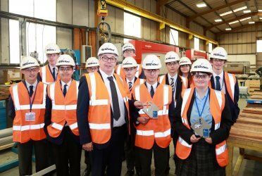 A group of people wearing hard hats and safety vests are standing in a warehouse.