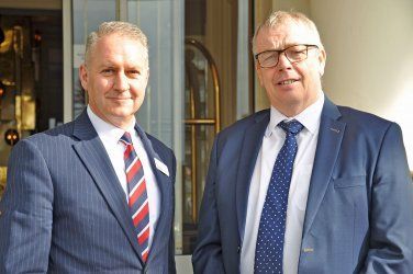 Two men in suits and ties are standing next to each other in front of a building.