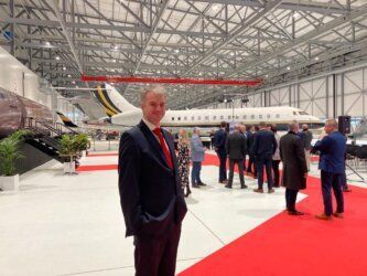 A man in a suit and tie is standing in front of an airplane in a  Reidsteel hangar.