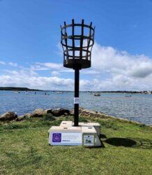 A statue of a torch is sitting on top of a grassy field next to a body of water.