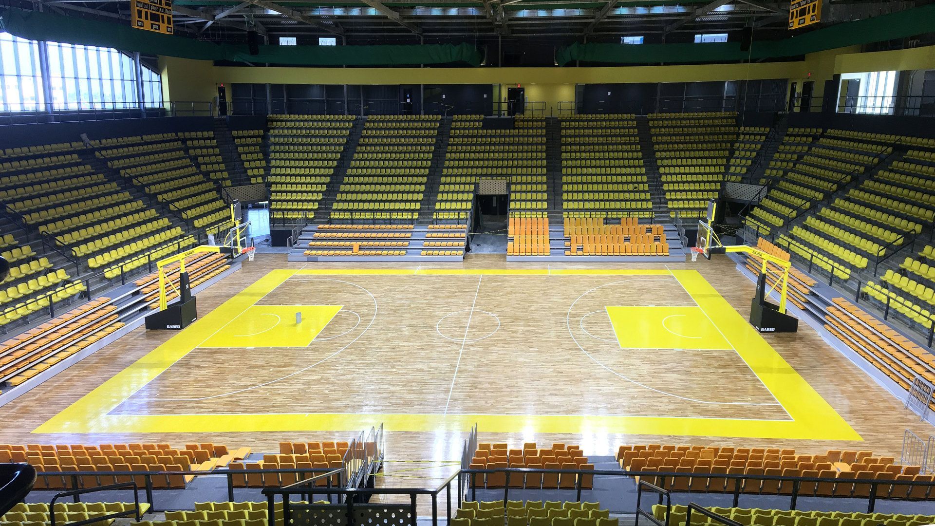 An empty basketball court in a stadium with yellow lines on the floor.