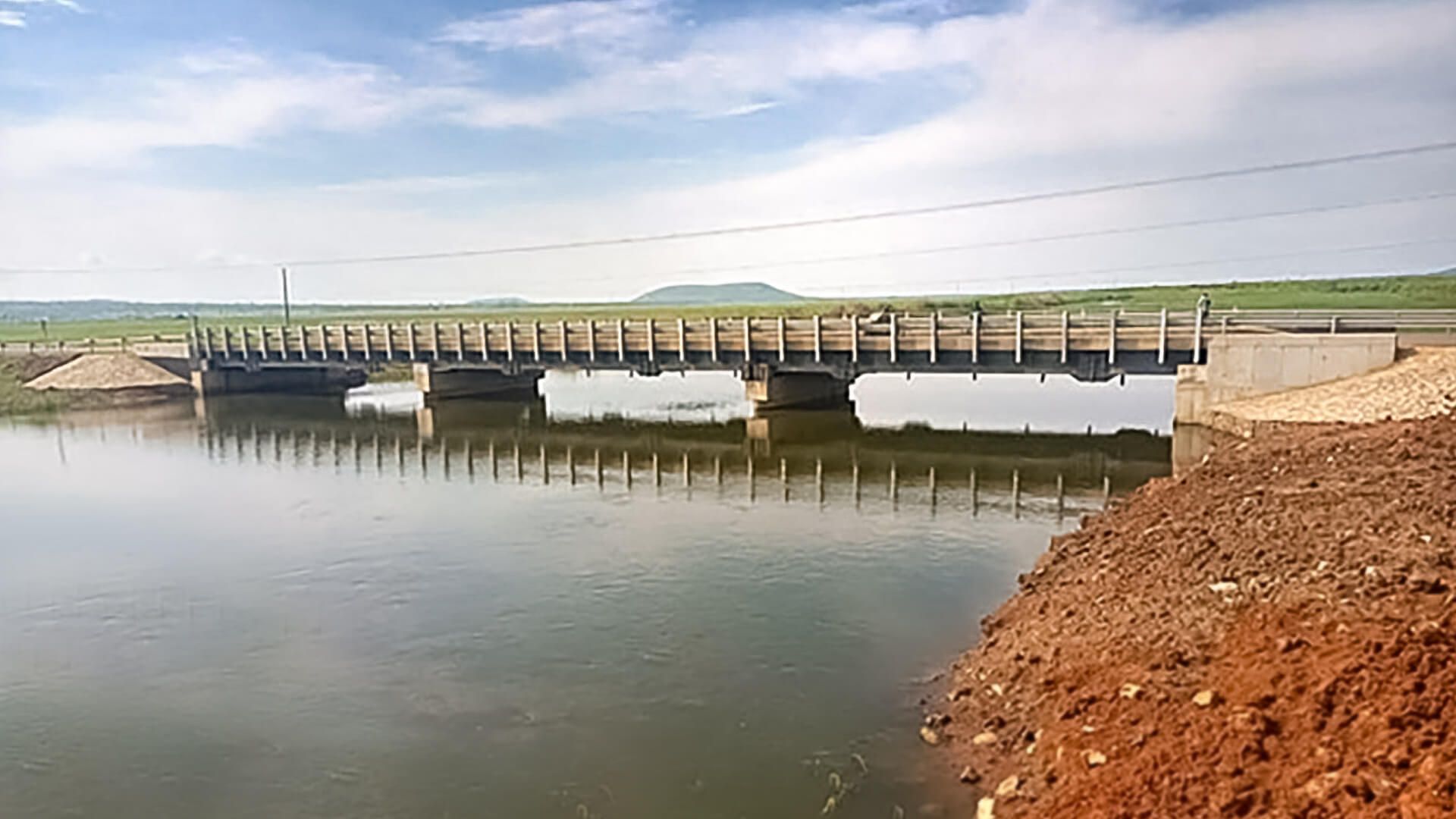 A bridge over a body of water in the middle of a field.
