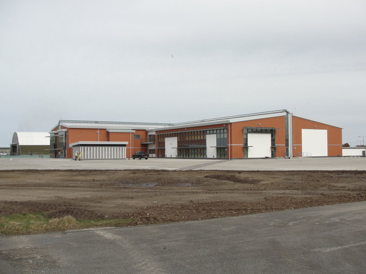 A large brick building with white doors is sitting in the middle of a dirt field.