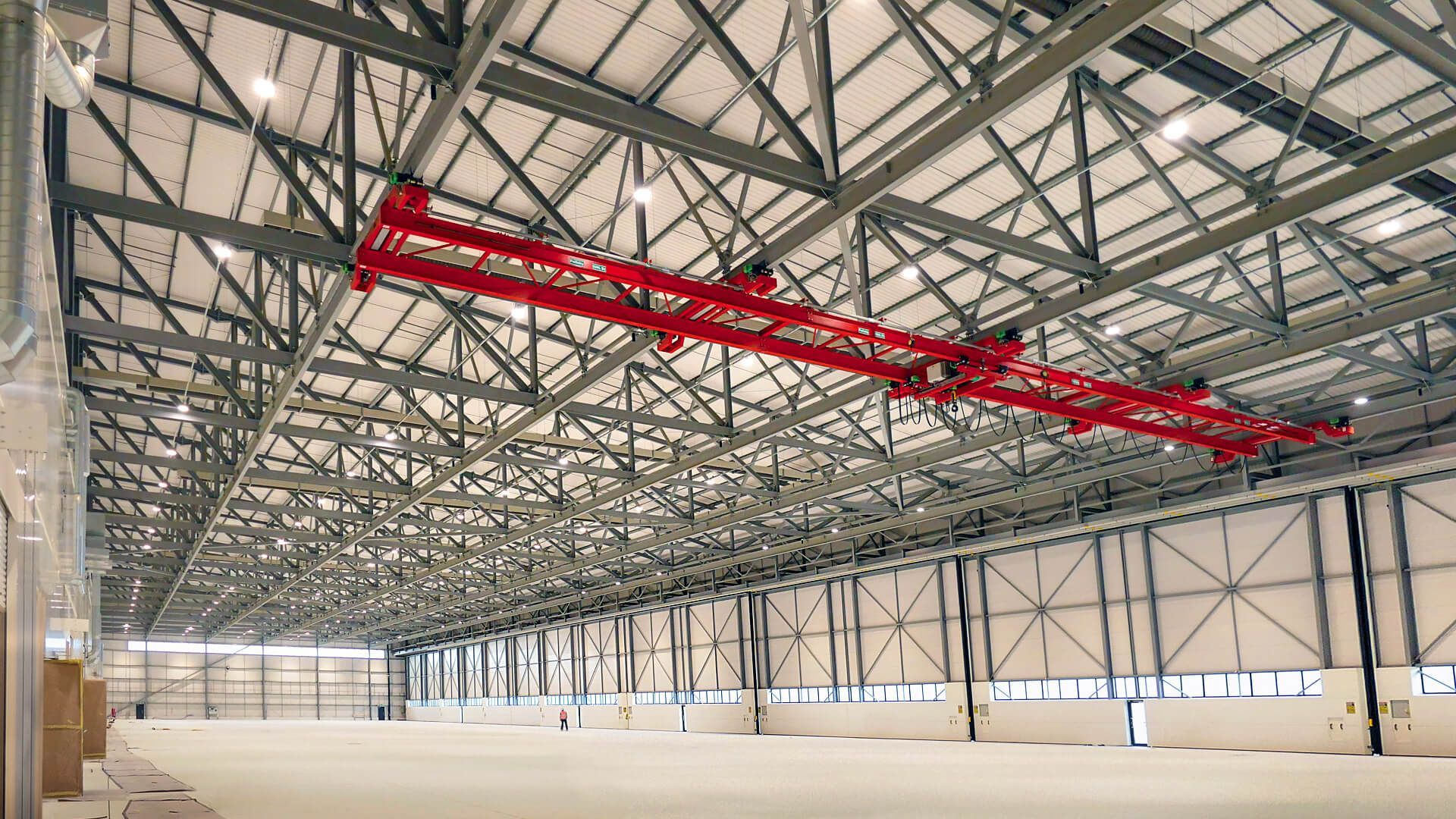 A large  aircraft hangar with a red crane hanging from the ceiling.