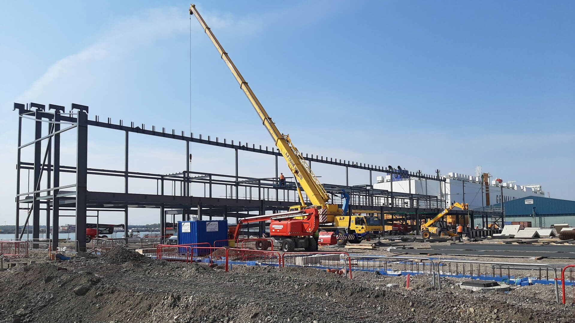 A large yellow crane is sitting in front of a large building under construction.