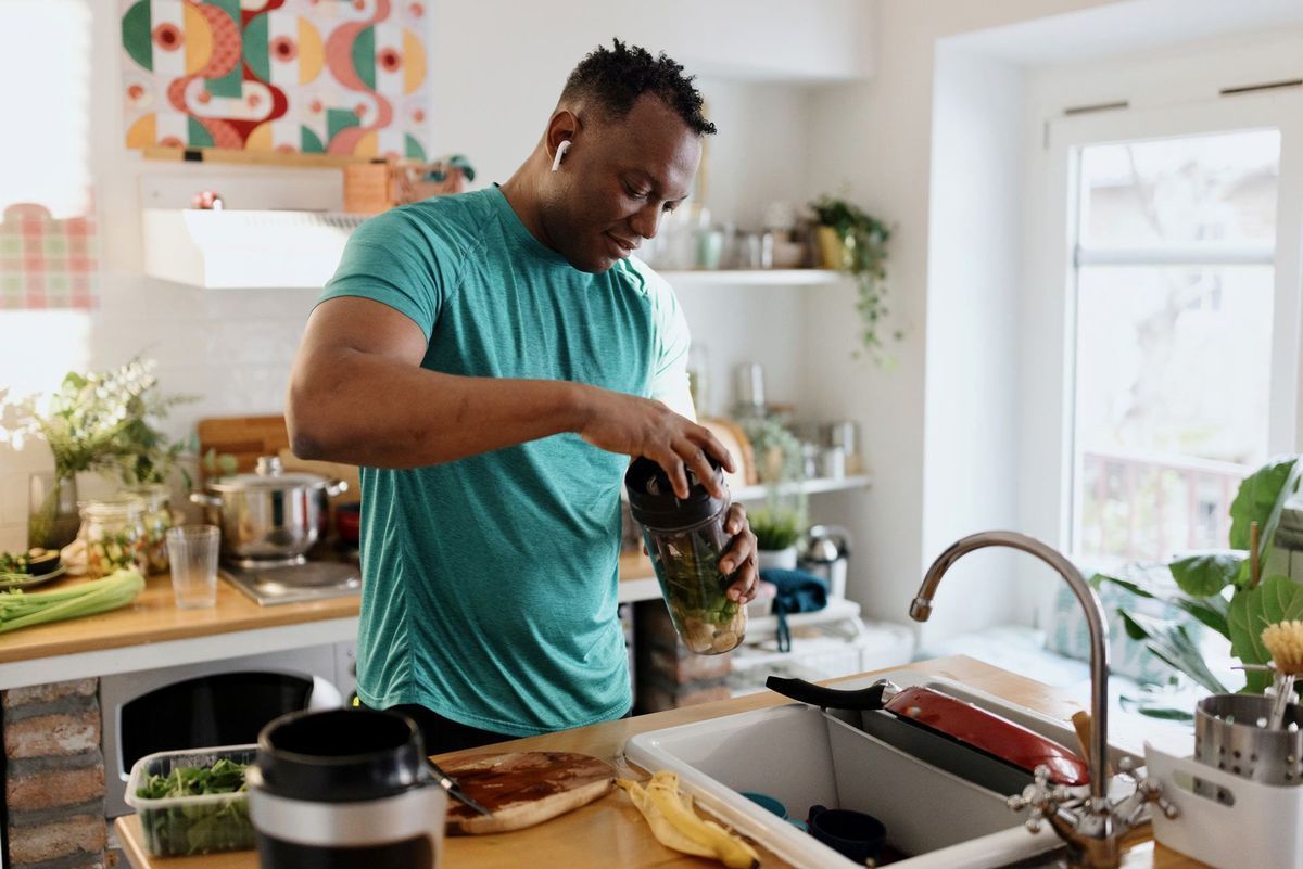 Man in green shirt prepares a smoothie in a kitchen.