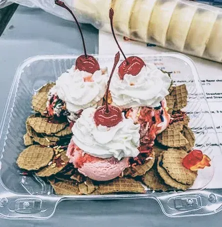Ice cream sundae in clear container with wafers, whipped cream, and cherries.