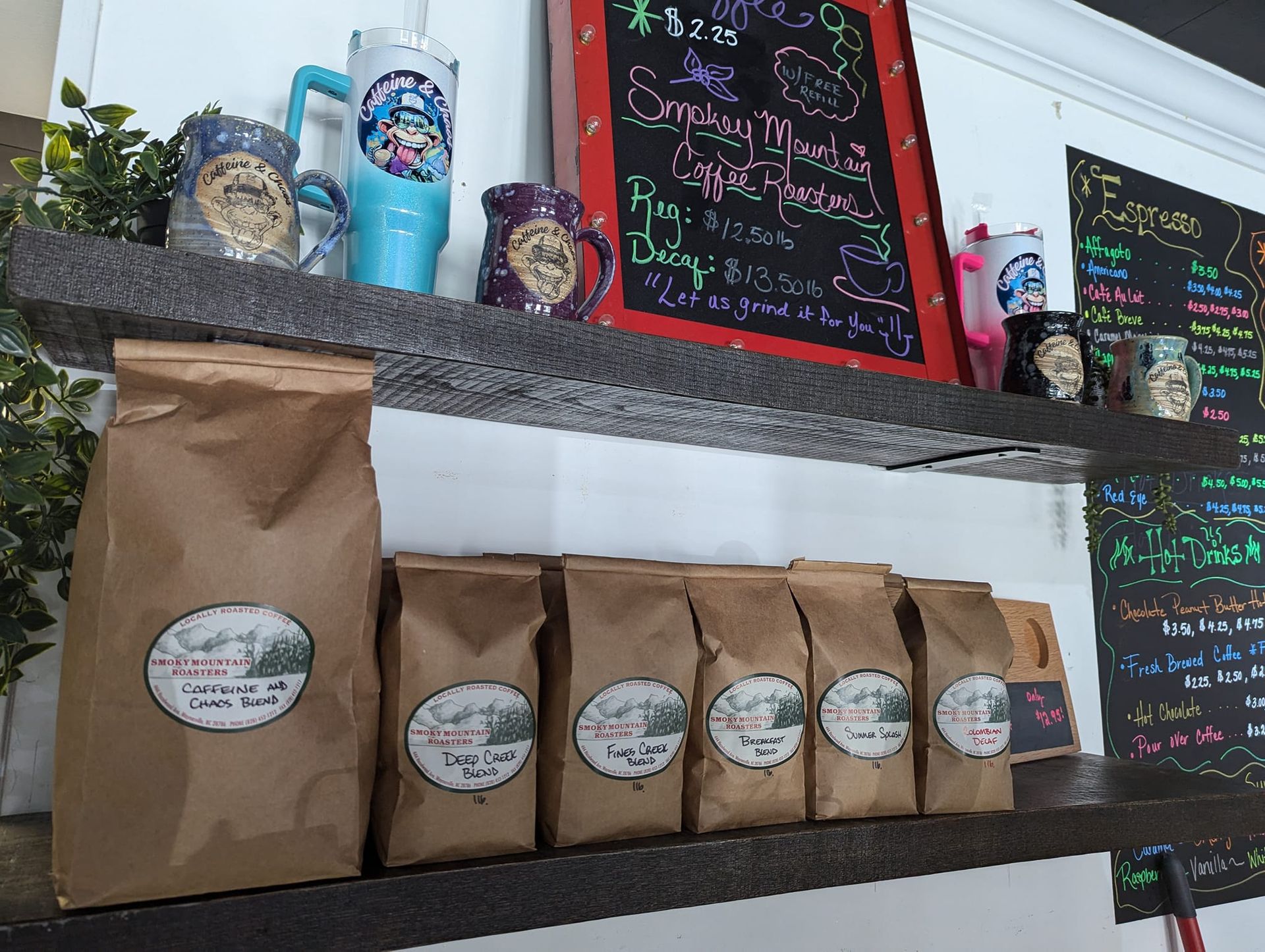 Coffee bags on a shelf with coffee mugs and a menu board in a cafe.
